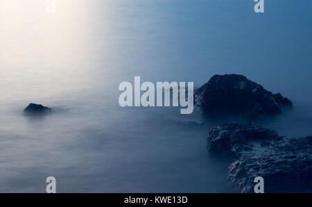 Le rocce che emergono dal mare sono illuminate dal sole al tramonto. Foto Stock