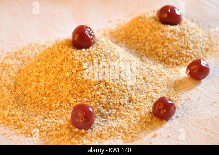 Due pile di chicchi di grano con conserve di ciliegie sullo sfondo di un sacco di close-up. Ingredienti per la cottura. Foto Stock