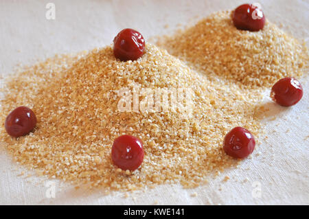 Due pile di chicchi di grano con conserve di ciliegie sullo sfondo di un sacco di close-up. Ingredienti per la cottura. Foto Stock