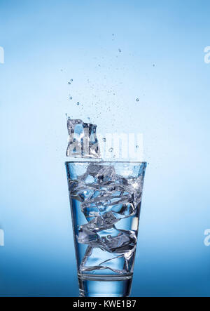 Gli spruzzi di acqua bicchiere con cubetti di ghiaccio su sfondo blu, closeup, vista frontale. Foto Stock