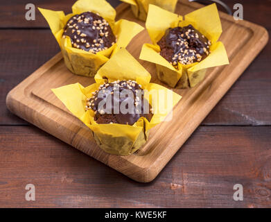 Il cioccolato muffin alla banana cosparso con noci e avvolto in carta gialla su una cucina in legno board Foto Stock