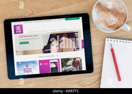 L'AIB (Allied Irish Bank) sito su un iPad dispositivo tablet, appoggiato su un tavolo di legno accanto a un blocco note, matita e tazza di caffè (editoriale solo) Foto Stock