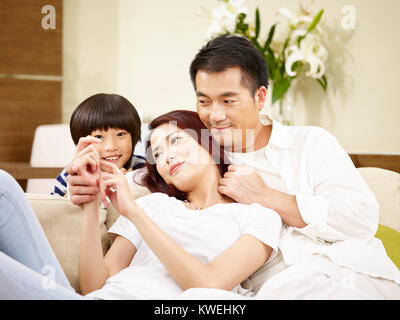 Asian madre padre e figlio godendo di una sessione di conversazione testuale in salotto. Foto Stock