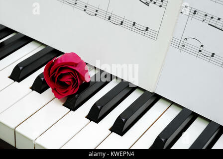 Red Rose e musica punteggio sulla tastiera di pianoforte, indicando di concetti come amore per la musica, di creatività e di amore e romanticismo. Foto Stock