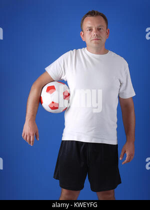 Giocatore di calcio indossando t-shirt bianco e nero shorts in posa con pallone da calcio su sfondo blu Foto Stock