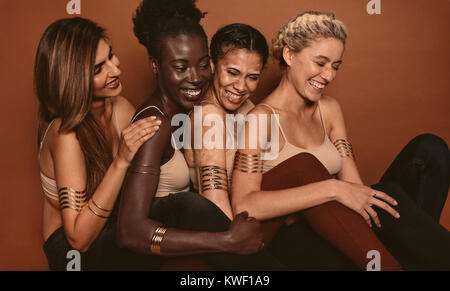 Donna sorridente modelli con diversi skin. Gruppo di multi etnico di donne giovani che cercano felice insieme su sfondo marrone. Foto Stock