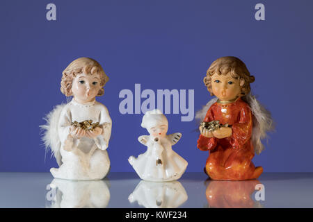Primo piano di tre angeli di porcellana, sfondo blu Foto Stock