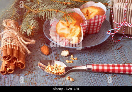 Limone mini muffin con decorazioni floreali in rosso-bianco carta su tavola in legno rustico con ramoscelli di Natale, mandorle e bastoncini di cannella. Immagine filtrata. Foto Stock