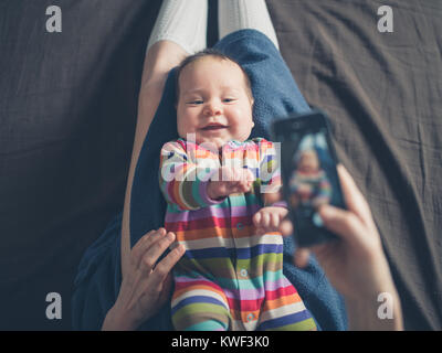 Una madre è utilizzando il proprio smartphone per scattare una foto del suo bambino Foto Stock