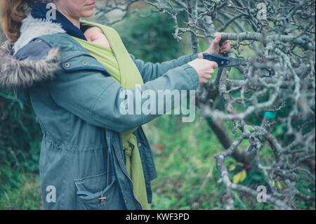 Una donna con un bambino in una imbracatura è il taglio di un albero con una sega Foto Stock