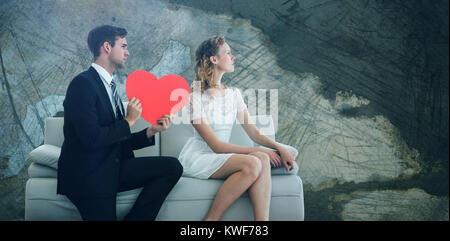 Immagine composita dell'uomo che mostra carta a forma di cuore rosso a. donna mentre si siede sul divano Foto Stock