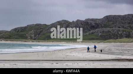 Due persone e un cane camminare sotto cieli grigi sulla spiaggia Reef, isola di Lewis, Ebridi Esterne, Scozia Foto Stock