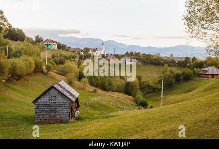 Magura village e la vista delle colline ai piedi delle montagne dei Carpazi in Piatra Craiului National Park, Transilvania, Romania, nella luce del mattino Foto Stock
