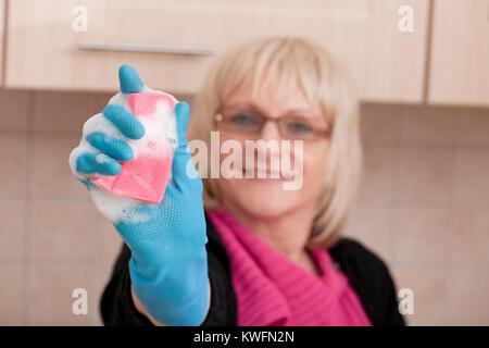 Casalinga matura tenendo una spugna schiumoso nella sua cucina. Focus sulla spugna! Foto Stock