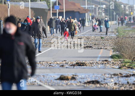 La gente che camminava sul lungomare durante una ruvida tempesta di neve nel gennaio 2018, con ghiaia dalla spiaggia e acqua di mare lavato fino sul percorso in Littlehampton, West Sussex, in Inghilterra, Regno Unito. Foto Stock