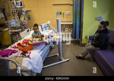 Iowa City, Iowa, USA. 31 ott 2017. Aria Defrates, 3, gioca con i giocattoli nel suo letto mentre la sua mamma, ambra, orologi dal lettino nella sua stanza presso la University of Iowa Stead famiglia ospedale per bambini a Iowa City il martedì 31 ottobre, 2017. Ambra Defrates, una madre single di quattro, è in cerca di aiuto per ottenere nuovi mobili come lei si muove in una townhouse. La mossa arriva dopo il suo appartamento con due camere da letto era infestata da cimici. Nella prima parte dell'anno Defrates ha perso il suo primo figlio, un 20-anno-vecchio figlia e solo recentemente la sua più giovane, tre-anno-vecchio aria, è stato diagnosticato un cancro del rene e Foto Stock