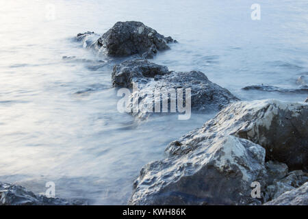 Le rocce che emergono dal mare sono illuminate dal sole al tramonto. Foto Stock