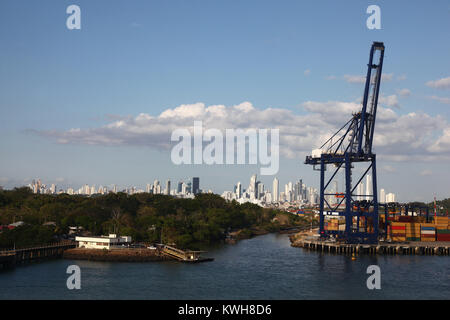 La porta di carico con gru e i contenitori di spedizione lungo l'ingresso del canale di Panama, con Panama city in background. Foto Stock