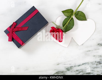 Single red rose su scheda con dark confezione regalo sulla pietra di marmo di sfondo piatto in vista dei laici Foto Stock