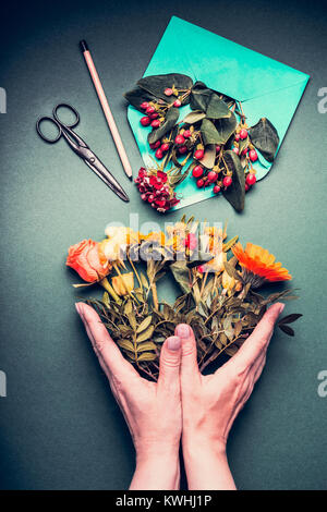 Mani femminili tenendo un Creative autunno bouquet di fiori su fioraio workspace sfondo tabella con aperto avvolgono , cesoie , matita, vista dall'alto. Invitat Foto Stock