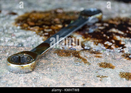 Una chiave a bussola da sinistra sul pavimento in una pozza di olio Foto Stock