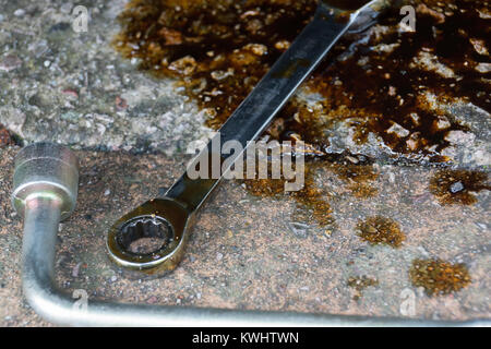 Una chiave a bussola da sinistra sul pavimento in una pozza di olio Foto Stock