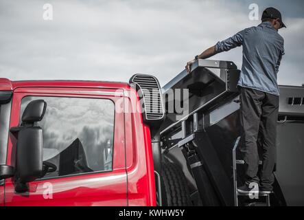 Autista del camion il controllo del carico nel suo autocarro con cassone ribaltabile. Per impieghi pesanti a tema di trasporto. Foto Stock