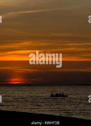 Tre pescatori in una piccola barca sull'oceano al tramonto Foto Stock