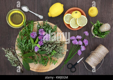 Condimento alle erbe con erbe fresche anche in fiore con limone e olio di oliva con stringa e forbici per appendere e foglie secche. Rustico in legno di quercia bac Foto Stock
