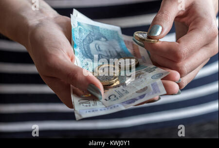 Primo piano delle mani di una donna in possesso di contanti, con banconote e monete di varie denominazioni di valuta britannica. Foto Stock