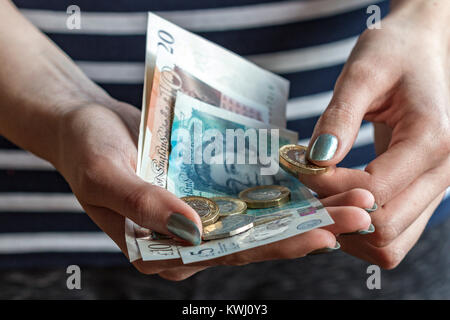 In prossimità di una donna di mano azienda Regno Unito valuta nella sua mano e un £1 moneta fra le dita,con le banconote e le monete di varie denominazioni Foto Stock