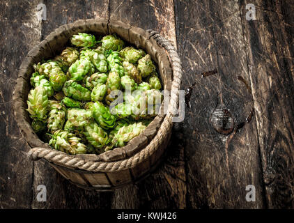 Il verde il luppolo per la birra in un secchio di legno. Su uno sfondo di legno. Foto Stock