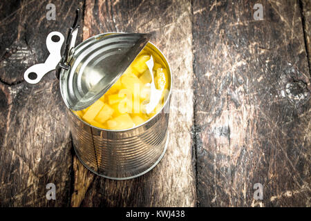 Aprire il barattolo di latta con ananas decapata. Su uno sfondo di legno. Foto Stock