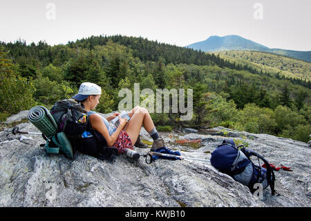 Escursionista in appoggio su sperone di roccia sul lungo sentiero, Vermont, USA. Cammelli gobba della montagna in distanza. Foto Stock