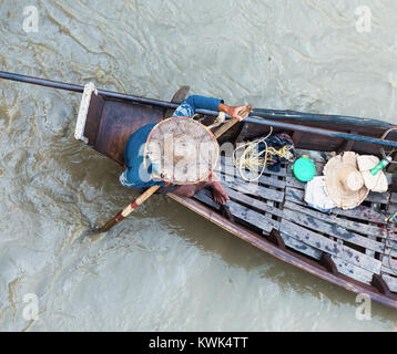 La prospettiva aerea della barca di legno tradizionale sul fiume Dala vicino a Yangon in Myanmar. L'uomo sulla barca indossa un molto usurati hat. Foto Stock