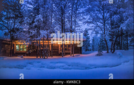 Romantic view of old traditional wooden forest cabin in the woods embedded in scenic northern winter wonderland scenery in beautiful mystic twilight Foto Stock