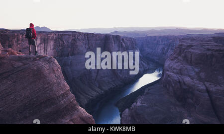 Un maschio di un escursionista è in piedi su ripide scogliere godendo della splendida vista del fiume Colorado che scorre alla famosa curva a ferro di cavallo si affacciano a mystic post tramonto Foto Stock