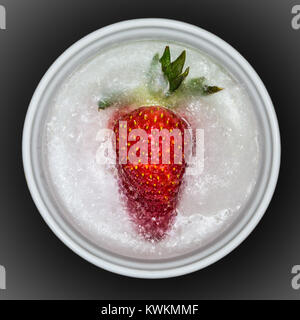 Un singolo fragole congelate in un piccolo white ramekin. Il frutto è coperto per metà dal ghiaccio. Foto Stock