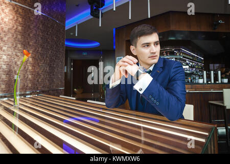 Bello sposo asiatica in un blu scuro tuta seduti nel ristorante e in attesa per la sposa, il concetto di un forte uomo di successo Foto Stock