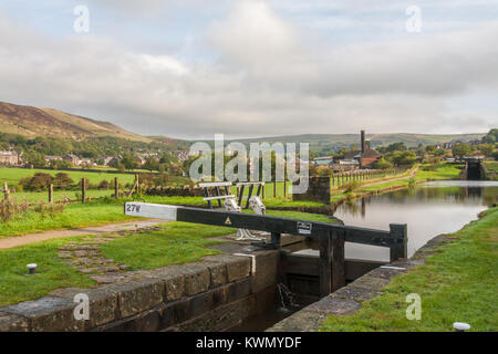 Bloccare il portellone 27 e cancelletto sul Huddersfield stretto canale con città in background, Diggle, Saddleworth, Oldham, England, Regno Unito Foto Stock