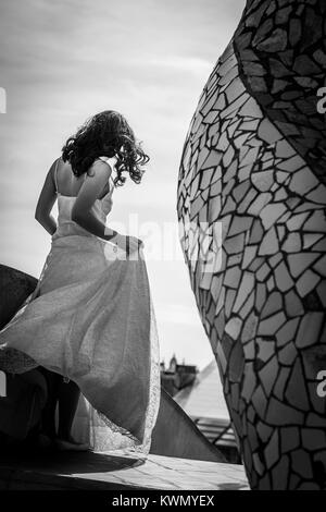 A basso angolo di vista posteriore di una giovane sposa con capelli ricci indossando un lungo senza maniche abito da sposa in attesa all'esterno contro il cielo nuvoloso Foto Stock