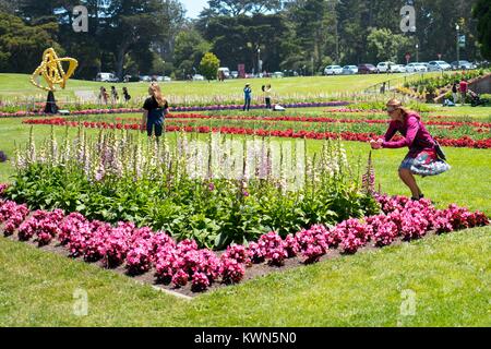 Un turista femminile si piega verso il basso per prendere un cellulare fotografia di un giardino formale presso il Conservatorio di fiori, un epoca vittoriana serra e al conservatorio di fiori in Golden Gate Park di San Francisco, California, 11 luglio, 2017. Foto Stock