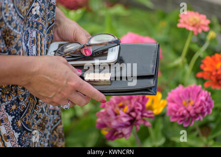 Primo piano della donna azienda wallet, bicchieri e smartphone in Summer Flower Garden Foto Stock