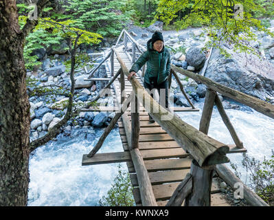 Trekker attraversando una passerella di legno in tutta Rio Ascencio; El Chileno camp site; Parco Nazionale Torres del Paine; Cile Foto Stock