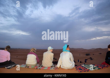 Turisti e dei berberi osservare il tramonto su una escursione in cammello alle dune di sabbia di Merzouga, Marocco, Africa del Nord Foto Stock