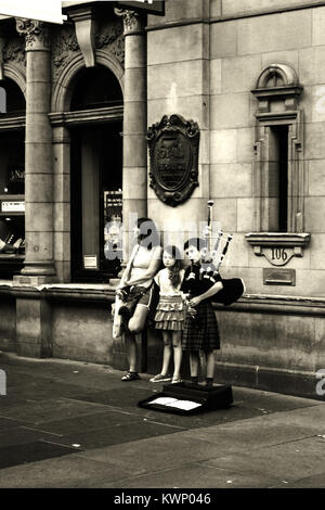 Bagpiper giovane ragazzo, con una donna e bambina, musicista di strada su Buchanan Street, Glasgow, Scozia Foto Stock