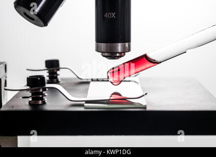 Pipetta contagocce, ponendo un rosso sangue gocciolina di sostanza su un microscopio e vetro per microscopio diapositiva, closeup, sfondo bianco macro retroilluminato Foto Stock