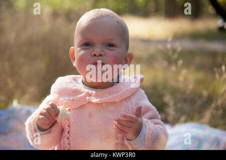 Bambina vestito in rosa maglione mangiare rullo bianco e sorridente. Foto Stock