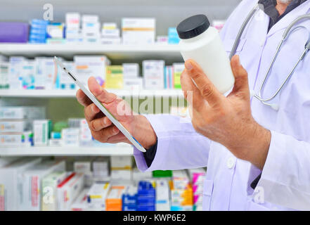 Il farmacista azienda medicina bottiglia e computer Tablet per il riempimento di prescrizione in farmacia farmacia. Foto Stock