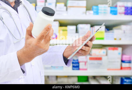 Il farmacista azienda medicina bottiglia e computer Tablet per il riempimento di prescrizione in farmacia farmacia. Foto Stock